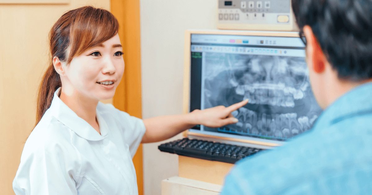 歯科衛生士が歯のレントゲン画像を指差しながら、患者に治療内容を説明している