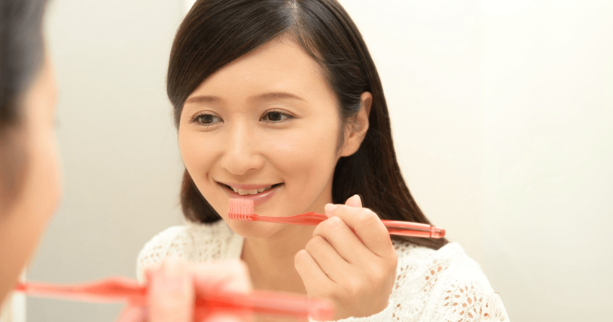 鏡を見ながら丁寧に歯を磨く女性の様子。毎日のセルフケアで歯痛予防。