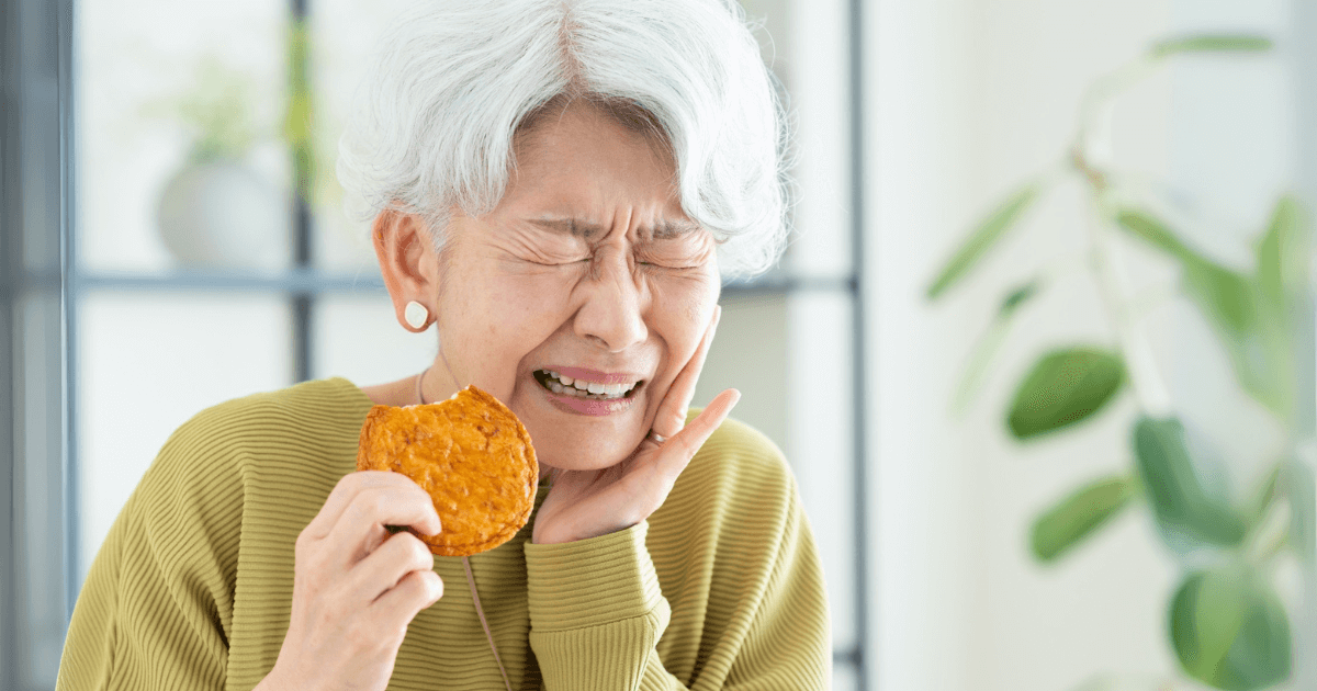 せんべいを食べた拍子に歯が欠けて痛みを感じている女性
