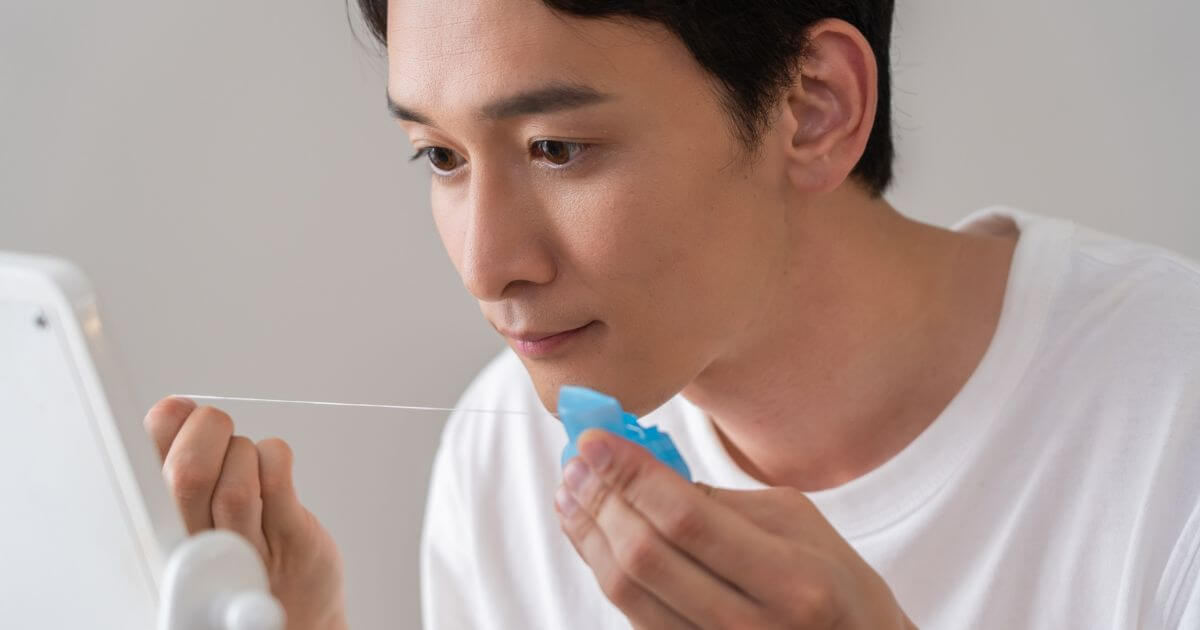 男性が鏡を見ながらデンタルフロスを使って歯と歯の間をケアしている様子