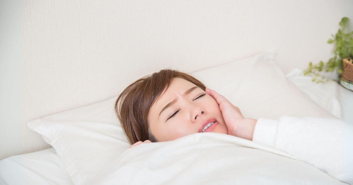 布団の中で歯の痛みに苦しむ女性