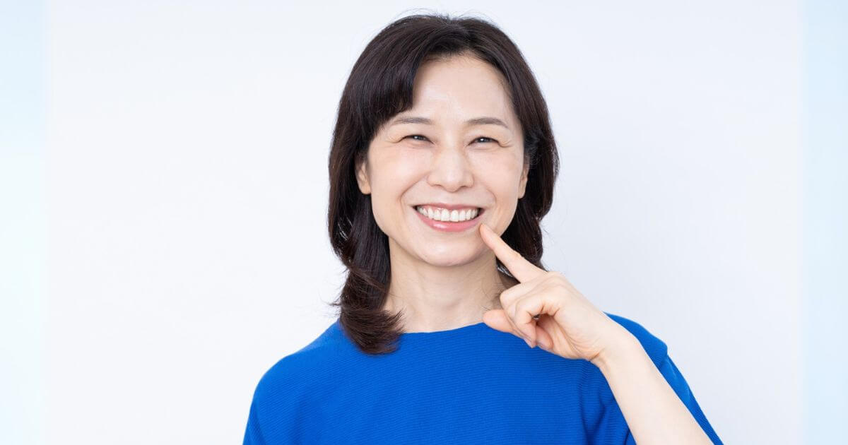 白い歯を見せて笑顔で口元を指さす女性