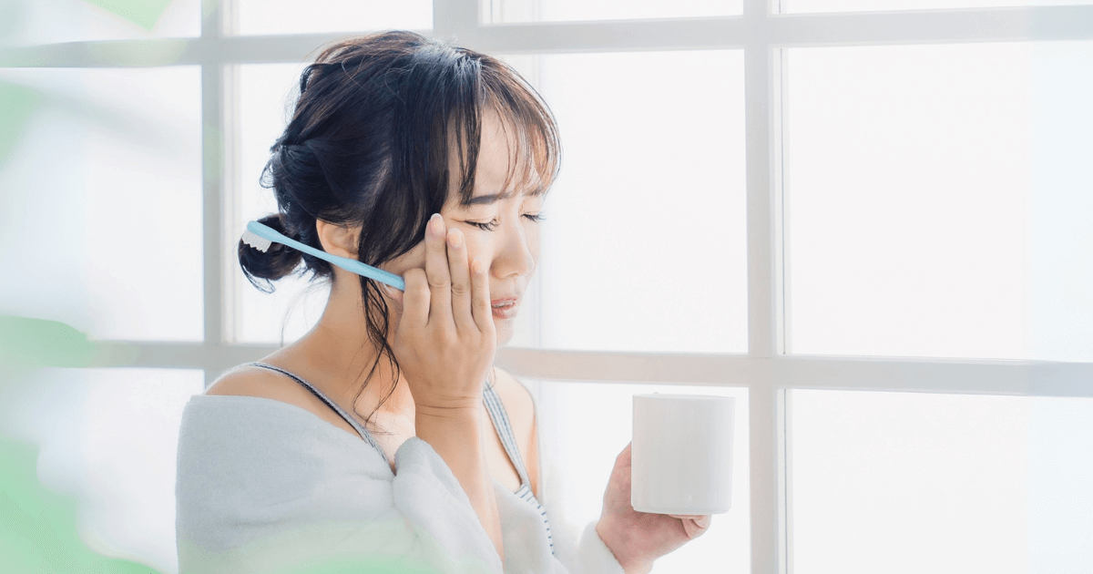 歯みがき中に歯の痛みを感じて頬を押さえる女性