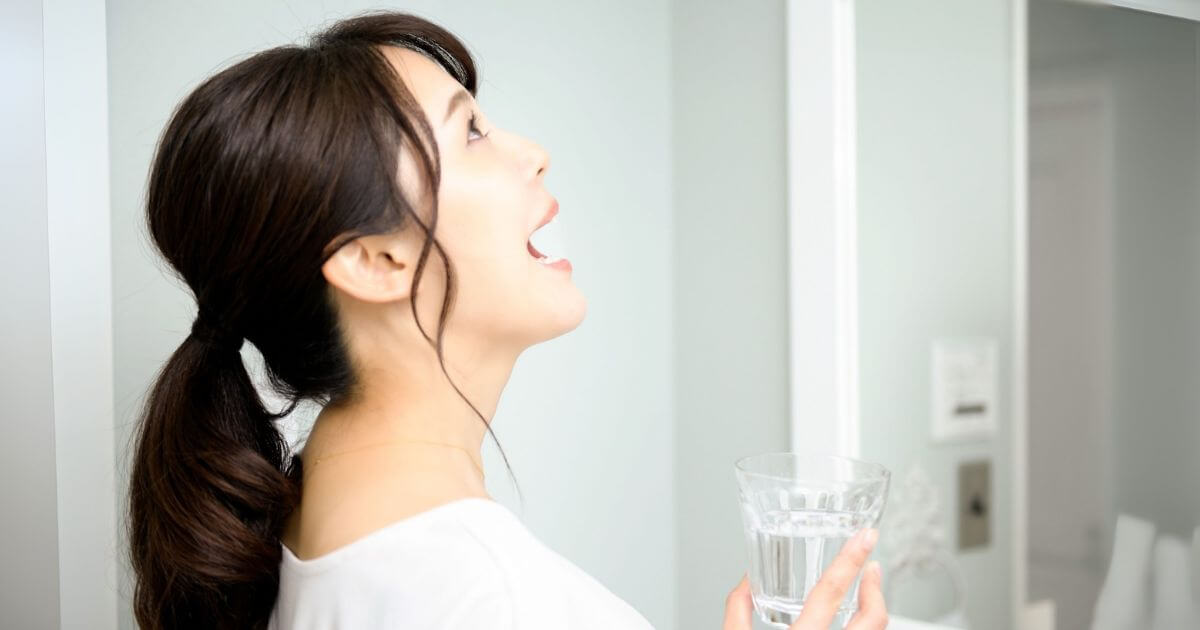 洗面所でコップの水を使ってうがいをする女性