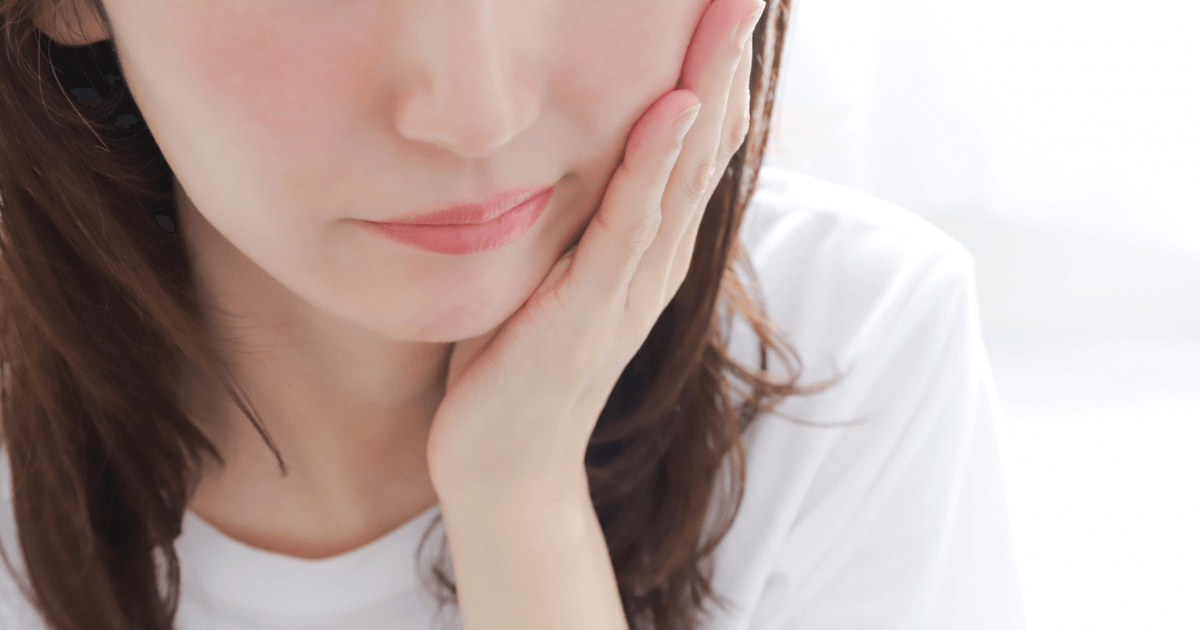 歯茎の痛みを気にして口元を押さえる女性
