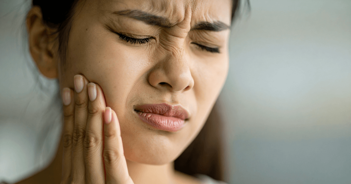 虫歯が悪化して頬を押さえ痛みを感じる女性