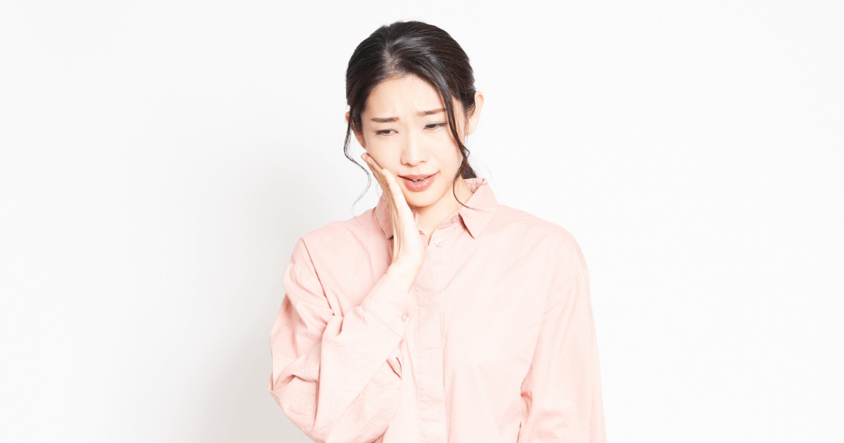奥歯や歯茎の痛みに悩む女性が頬を押さえている様子