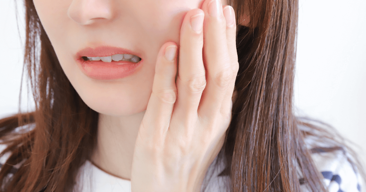 抜歯後に強い痛みを感じて頬を押さえる女性のイメージ