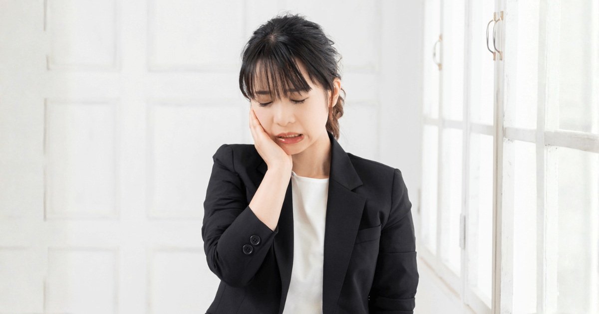 片方の頬が腫れて痛みを感じ、手で押さえる女性。虫歯や炎症などの原因を示すイメージ。