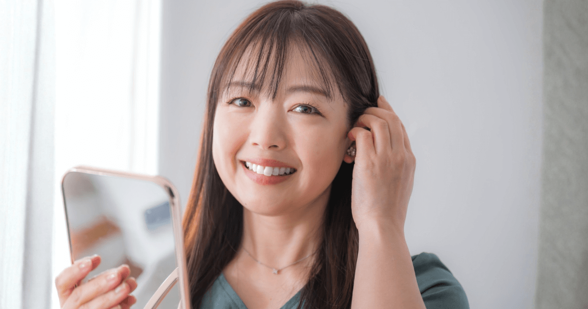 鏡を手に持ち、笑顔で頬の状態を確認する女性。腫れが治まり安心した様子を表すイメージ。