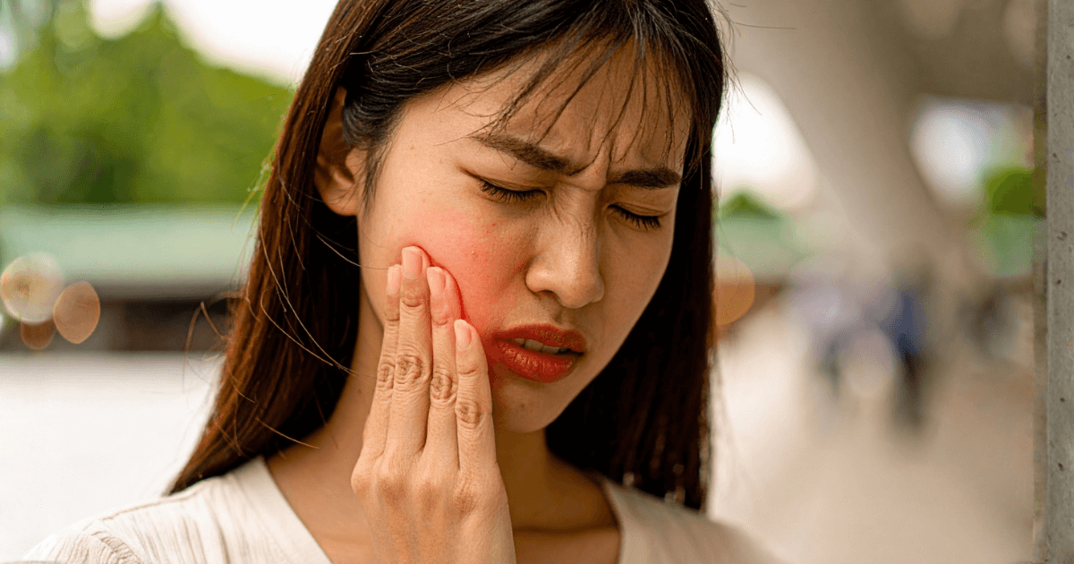 頬の炎症による強い痛みで顔を押さえる女性。腫れを放置したときのリスクを表すイメージ。