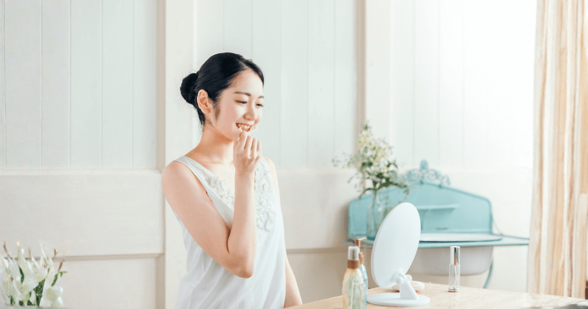 鏡の前でデンタルフロスを使う女性。口腔ケアによる頬の腫れ予防をイメージした写真