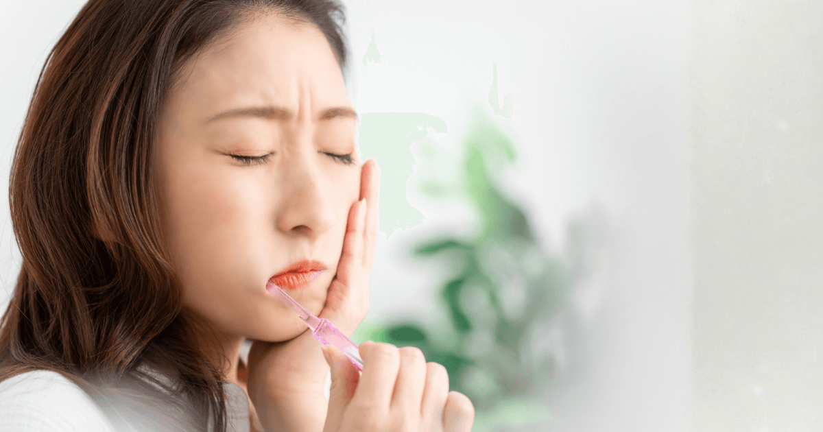歯の痛みを感じて頬を押さえる女性のイメージ。インプラント手術後の痛みを和らげるケアを意識している様子。