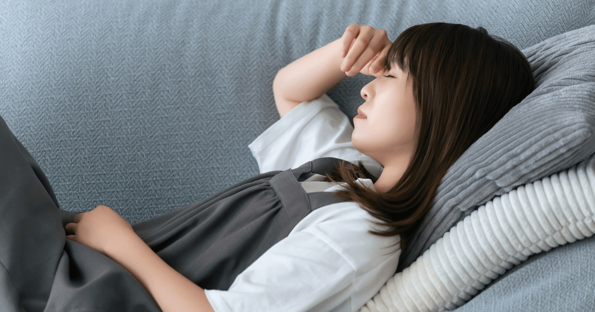 体調不良で横になりながら顔を押さえる女性のイメージ。インプラント手術後の異常な痛みや発熱など、受診が必要なサインを示している。