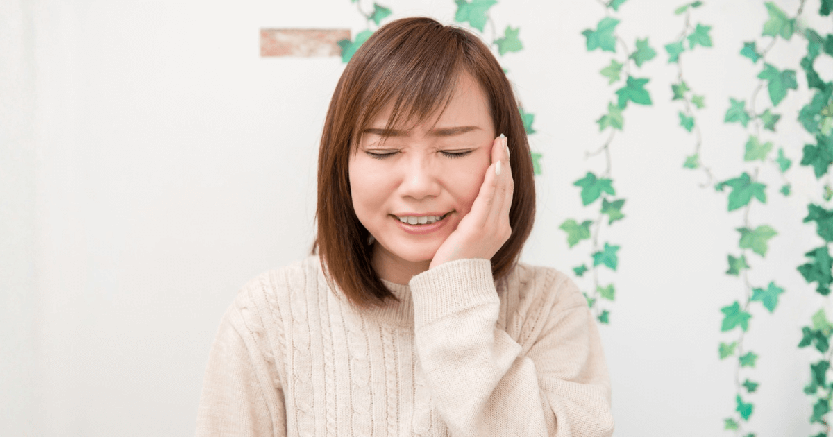 抜歯後の痛みで頬を押さえて受診を検討している女性のイメージ