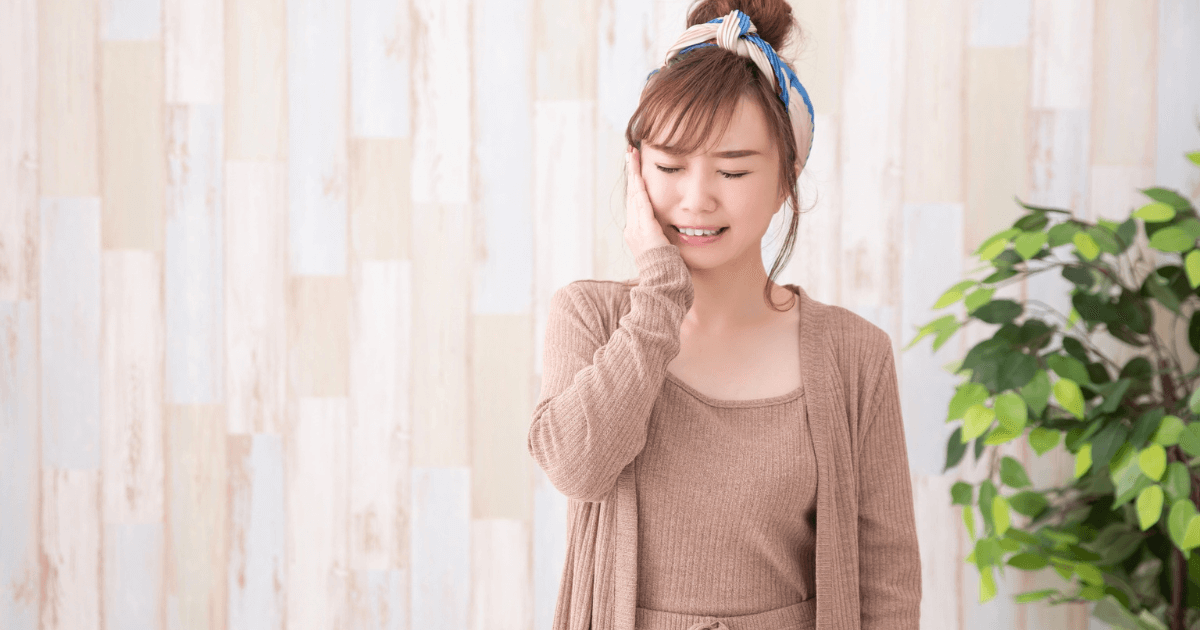 頬に手を当てて歯茎の腫れや痛みを気にする女性のイメージ写真