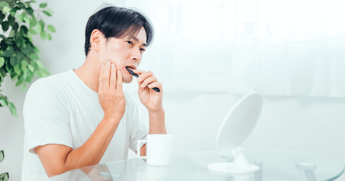 歯に違和感を覚え、鏡を見ながら口元を確認する大人の男性