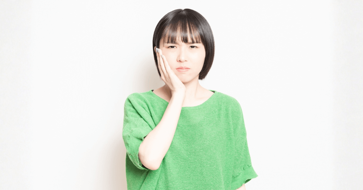抜歯後に頬を押さえて痛みを感じている女性のイメージ