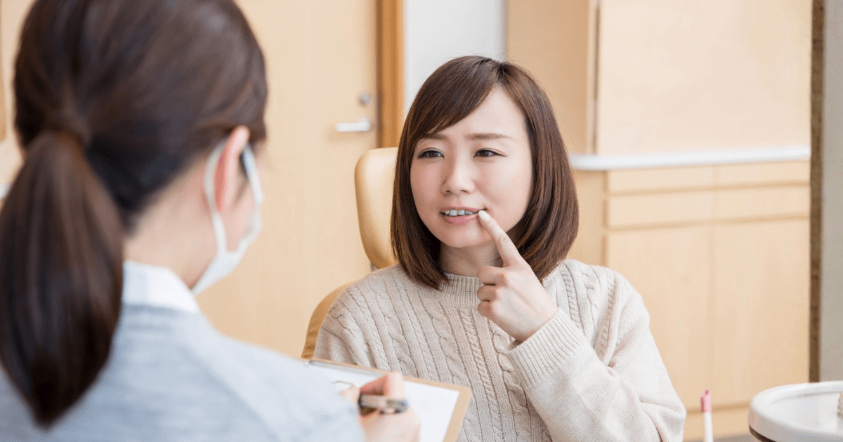 歯の症状を指しながら歯科医師に相談する女性のイメージ