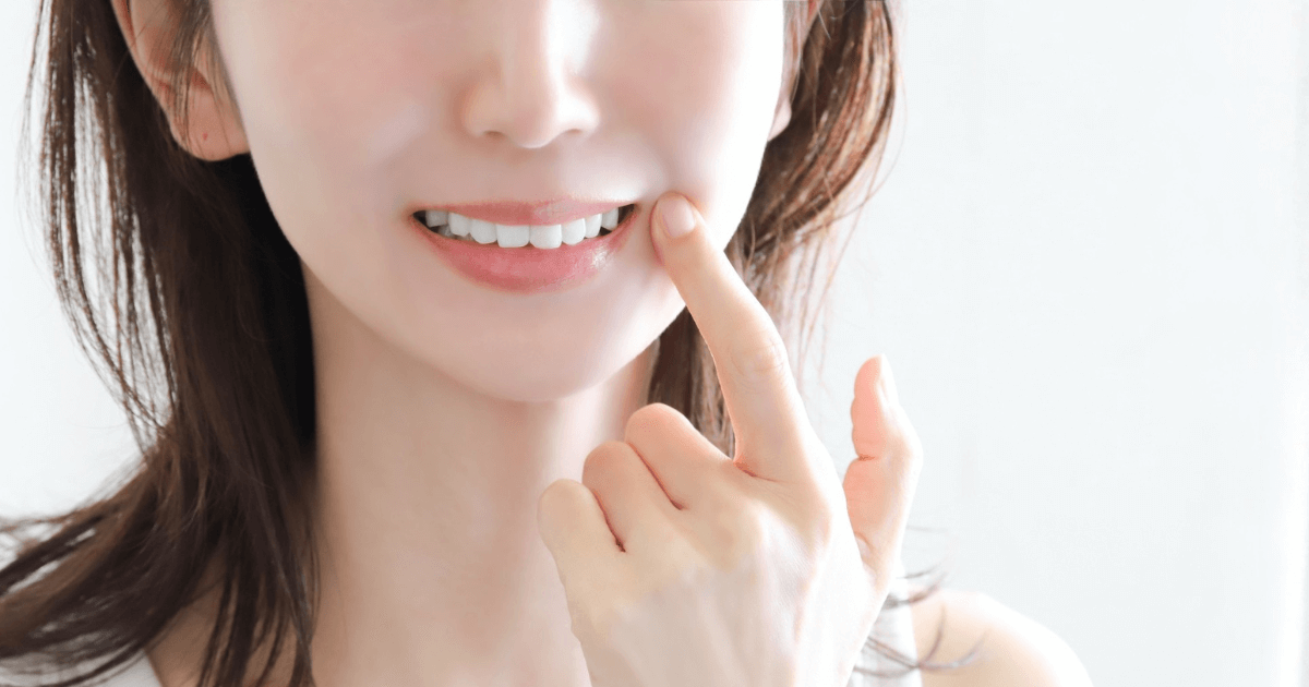 白い歯を指さして笑顔を見せる女性のイメージ