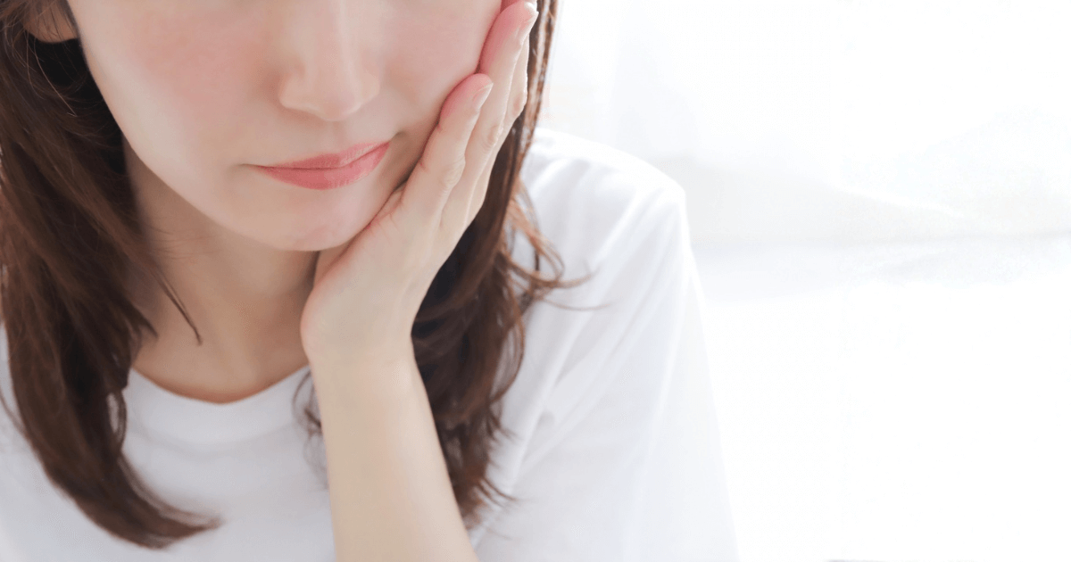 虫歯を触ると痛みを感じて頬に手を当てる女性のイメージ