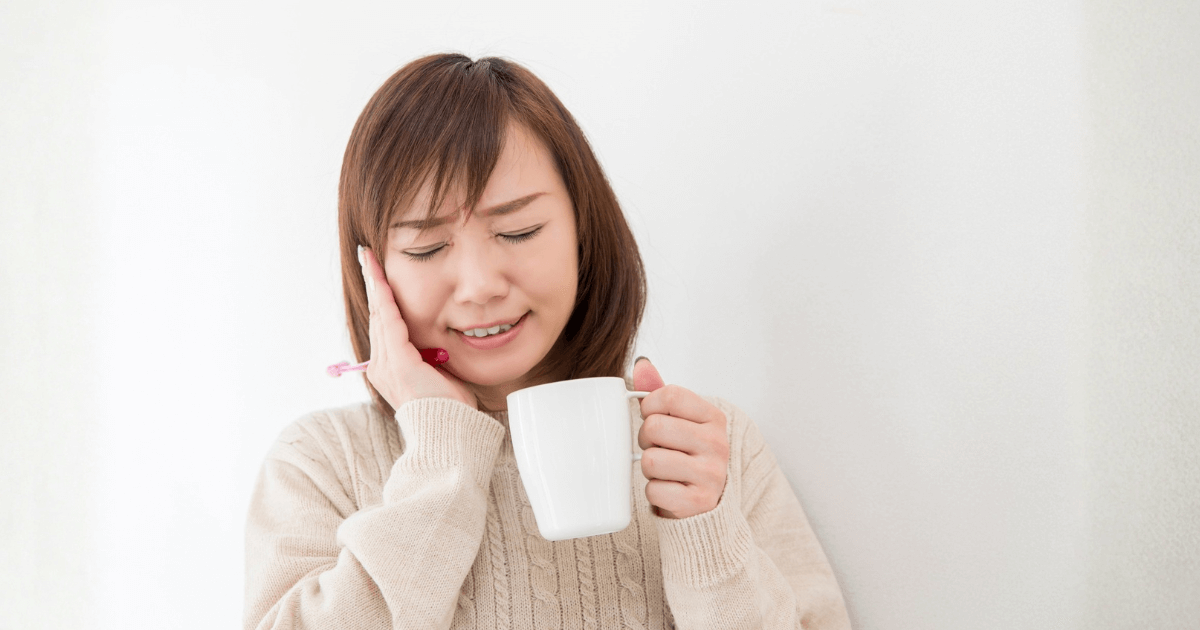 強い歯の痛みで頬を押さえる女性の写真。抜歯が必要なサインを示すイメージ