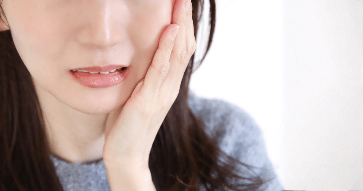 抜歯後に痛みや違和感があり、歯の欠片が残っているか不安を感じて頬に触れる女性のイメージ