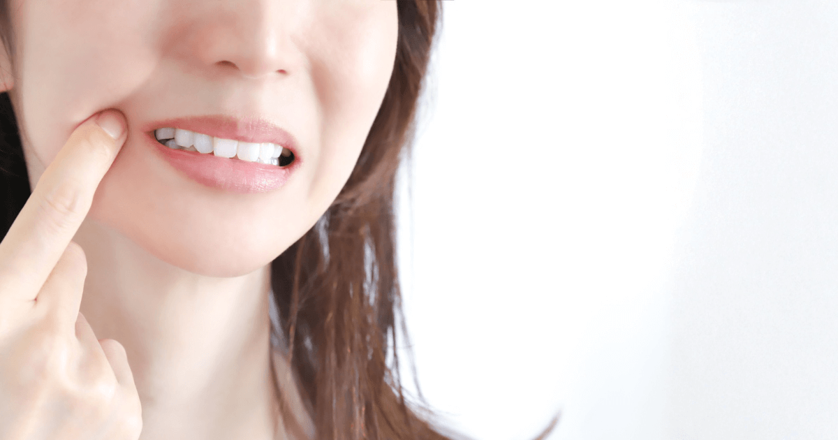 奥歯の痛みや不調を心配してほほを押さえる女性の口元