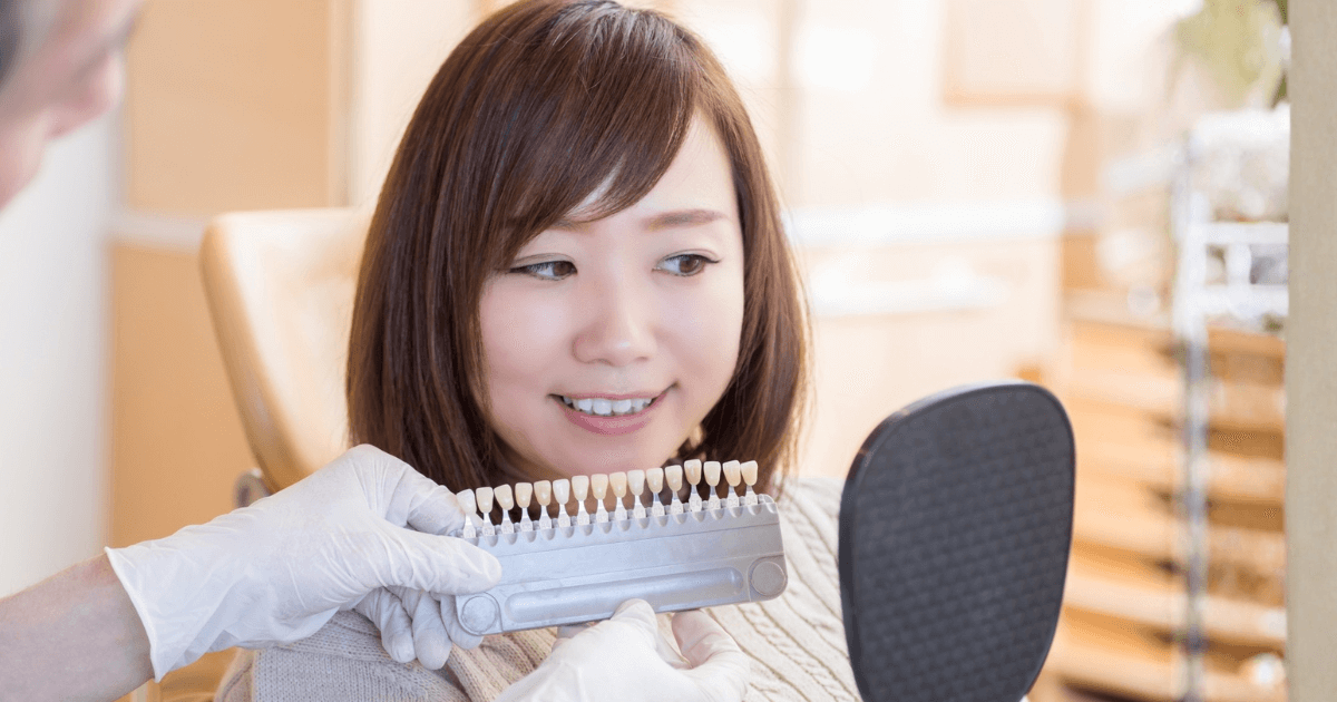 歯科医院で歯の色見本を見ながら治療方法を相談する女性